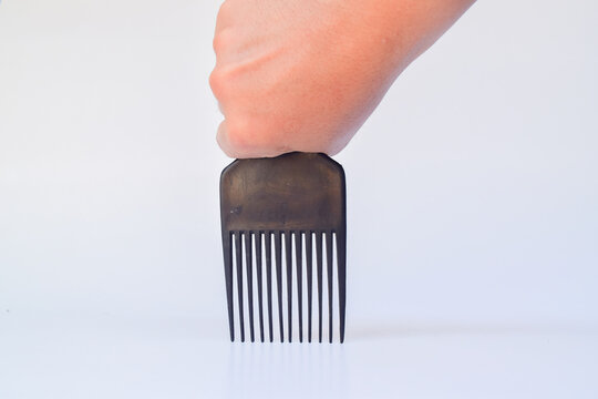Hand holding a vintage afro pick comb tool for textured hair styling, studio lighting against a clean white background in a close-up overhead shot
