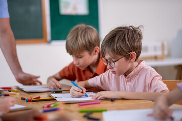 Fototapeta premium Teacher Helping Elementary Students with Drawing Activity in Classroom. Creative Classroom Lesson with Kids Coloring and Drawing, Education and Child Development in Modern Setting with boy, girl.