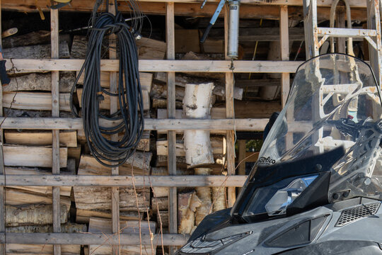 Canada, 11 April 2026 : BRP Ski-Doo snowmobile with Nautico windshield parked near a woodpile and grease gun