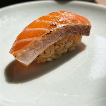 Close-up of a single torched salmon nigiri sushi on a white ceramic plate with dramatic shadows. Premium Japanese cuisine, aburi salmon sushi photography.
