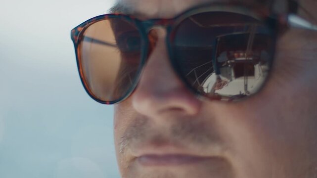 Close up portrait of the young man wearing sunglasses with reflection of the sailing boat. Person sailing, boat reflects in his sunglasses