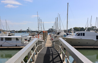 Fototapeta premium Metal gangway leading to a long pontoon lined with motorboats and yachts at the Gladstone Marina under a clear blue sky in Queensland, Australia