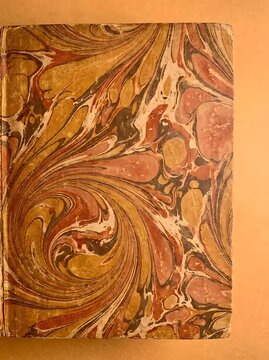 Close-up of a vintage book cover featuring an intricate, swirling marbled paper design in warm tones of gold, brown, and reddish-brown.