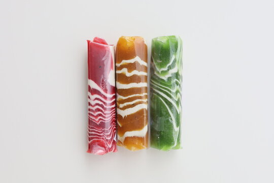 Three pieces of Dodol Garut, traditional Indonesian sweet taffy, with colorful striped patterns in red, green, and brown, isolated on a white background.
