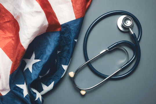 Stethoscope on Grey Background Next to Crumpled American Flag Representing United States Healthcare System and Medical Policy