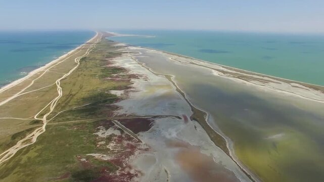 An aerial view showing the narrow sand spit separating the calm sea from the vast open blue ocean