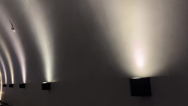 Minimalist lamps casts soft glow on textured wall. Dark base contrasts with warm, diffused light above. Ideal for serene, modern interiors or mood lighting scenes. No people, nobody. copy space, empty