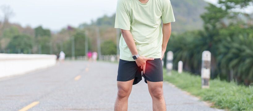 Young adult male runner suffering from acute groin pull and muscle pain during running workout. Man holding his inner thigh due to sports injury and strain. Medical and healthcare concept