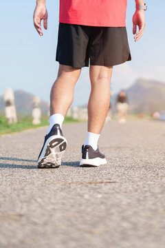 Young adult Asian man jogging and walking in the park at morning. male athlete in sport shoes running on the road with visible leg muscles. Healthy lifestyle, wellness and workout concept
