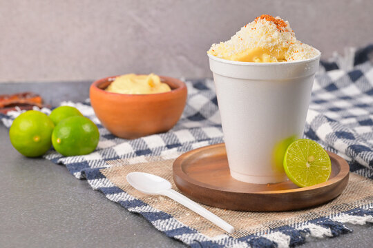 Traditional esquites in styrofoam cup on rustic background with fresh limes
