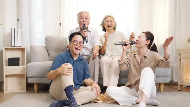 Happy multi-generation Asian family singing karaoke together at home, senior parent and adult child enjoy and fun leisure activity in living room, family bonding, happiness joyful retirement lifestyle