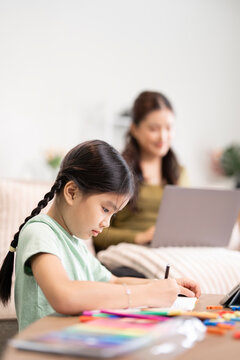 Asian girl doing homework with mother working on laptop