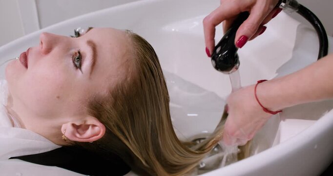 Hairstylist rinsing. Professional service. Experienced master hands providing treatment for female client strands in beauty salon.