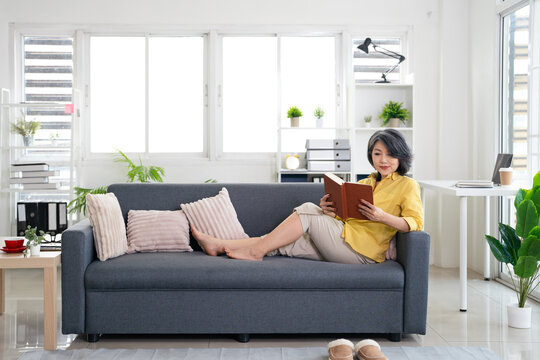 Aged woman sitting on couch and reading book pastime . senior lady enjoying free time at home.