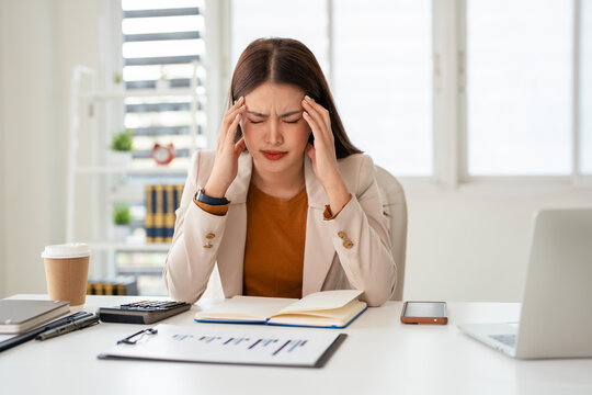 Young asian business woman feeling stress and tired from work sitting on the chair about constant headaches a migraine of working hard at office.