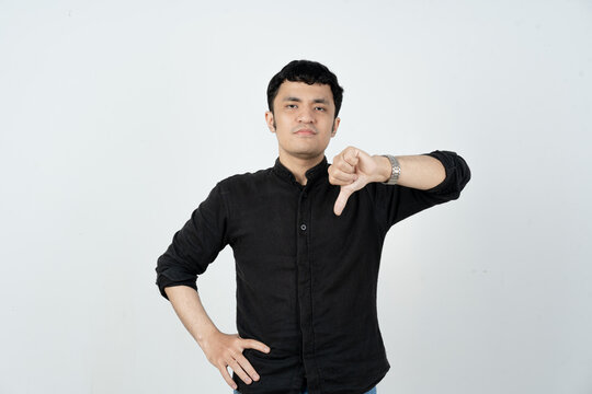 Portrait of Asian man gesturing thumbs down expressing dislike and negative feedback
