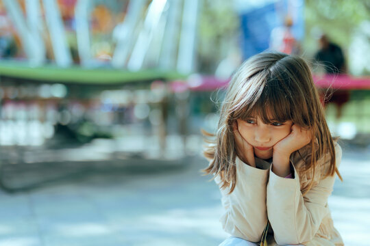 Sad Girl Sitting Facing Away the Trampoline in Amusement Park. Unhappy solitary child feeling lonely and being disappointed