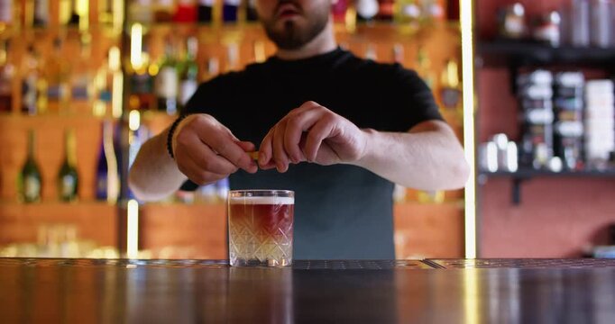 Fresh cocktail. Alcohol beverage. Professional bearded male barman serving decoration with lemon spiral zest cherry at bar counter.