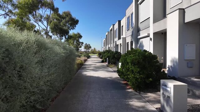 Modern two-story townhouses adjacent to a landscaped pedestrian walking path and native gardens in an outer suburb of Melbourne Australia. A wide footpath, and organized suburban housing layouts.