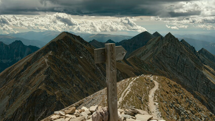 Wooden signpost marker on rocky mountain peak summit ridge trail with cloudy dramatic sky, hiking trekking outdoor adventure travel and direction choice concept © Lumi Stock Studio