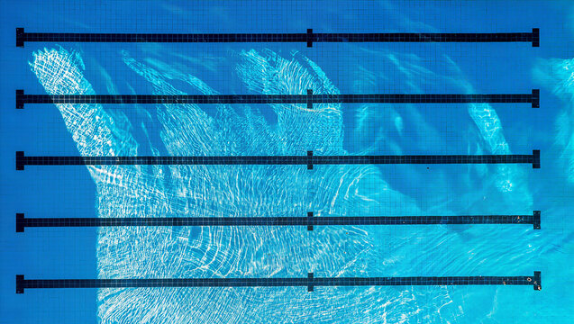 Aerial top view of empty blue swimming pool with lane lines and clear rippled water surface, sports competition training facility and summer vacation background