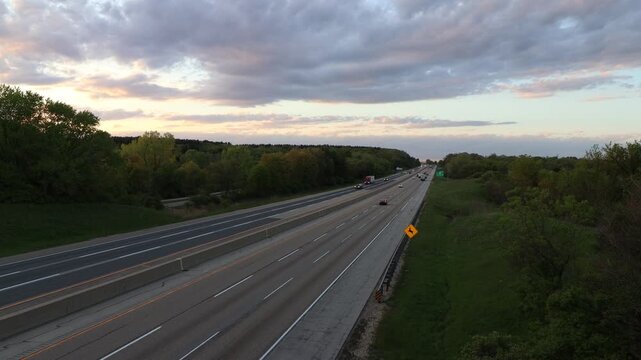 Cars and semi trucks drive down a long interstate highway road into the horizon in the top right third of the screen during a nice sunset.