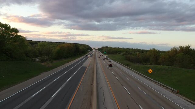 Cars and semi trucks drive down a long interstate highway road into the horizon in the middle of the screen.