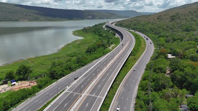 Aerial view of highway running along river and green hills. Transportation, infrastructure, travel and logistics concept