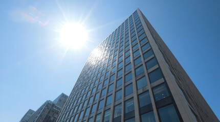 Fototapeta premium Modern glass office tower with bright sun glare and clear blue sky, dramatic midday light
