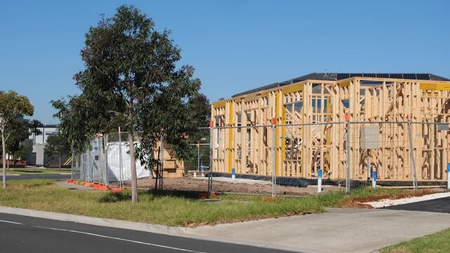 A timber-framed residential building under construction in a newly developing suburb of Melbourne, Victoria, Australia, with temporary security fencing, eucalyptus trees on nature strip.