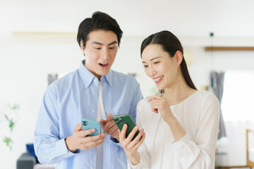 Fototapeta premium リビングでスマホを持って会話する若い日本人セレブカップル