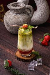 a glass of strawberry matcha drink containing strawberry jam, full cream milk, matcha and strawberries with strawberry and mint leaf decoration on a wooden coaster © kitapoto