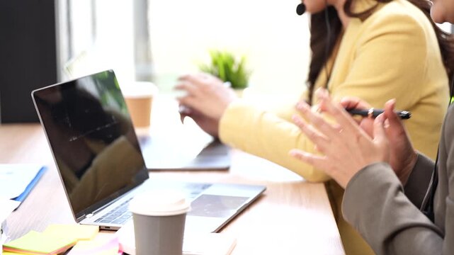 Two Asian female customer service agents with headsets talking with customer vai laptops in a modern office.