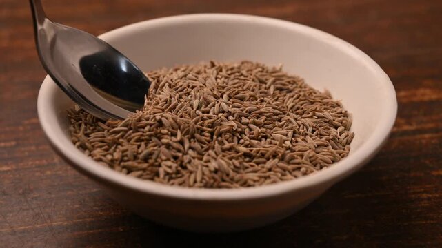 Cinematic Macro Shot of Cumin Seeds in Spoon from Bowl on Table &ndash; Angled Top View with Soft Blurred Background, 4K Food Stock Footage