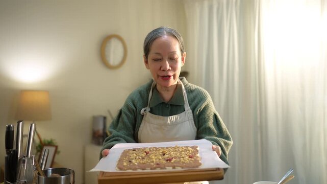 Senior woman livestreams cooking from home on smartphone, highlighting active aging and digital lifestyle. Reflects social media, content creation, creativity, and senior lifestyle.