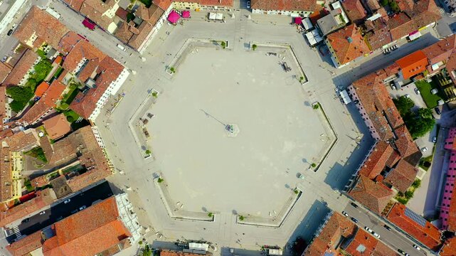 Palmanova, Udine, Italy. Aerial top-down view of the hexagonal Piazza Grande at the center of the nine-pointed star fortress, with terracotta rooftops radiating outward under bright midday sun. Drone