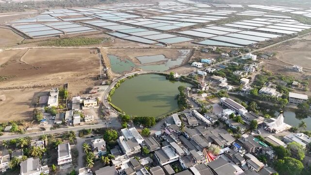 A breathtaking aerial view of expansive salt evaporation ponds spread across a dry coastal landscape near a rural village.
