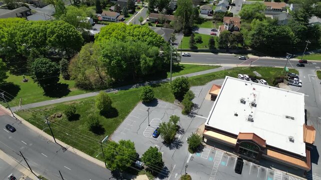 High-altitude drone footage capturing a large commercial building with a flat roof and an expansive parking lot in a suburban area.