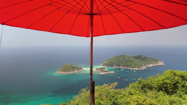Large red umbrella provides shade over lush tropical island view and turquoise sea