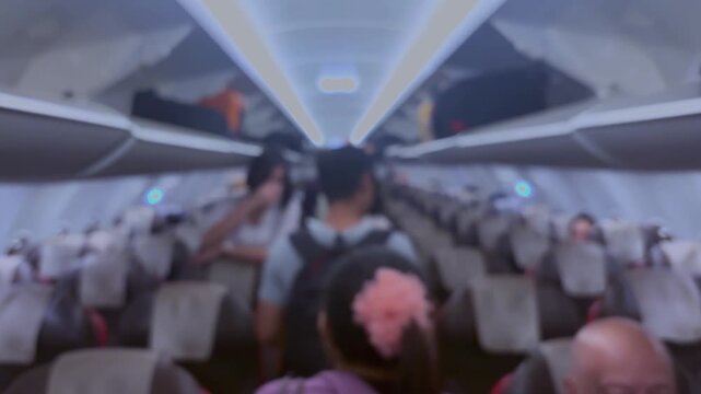 Passengers are walking inside the aircraft cabin, while looking for their seat numbers and putting their luggage into the cabin.