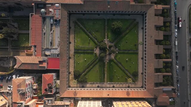 Symmetrical courtyard garden of Chiostro di Michelangelo with pathways and central tree inside historic building complex, aerial