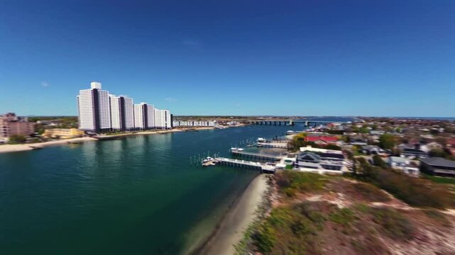 An FPV drone view over Reynolds Channel by the Sand Castle Oceanfront Living apartments on a sunny day. The camera dolly out, pan right 180 degrees showing the beautiful waterfront scenery.