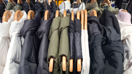 Row of warm winter puffer jackets and quilted coats hanging on wooden hangers in a retail fashion store with focus on padded textile texture for outdoor apparel concept © Rungphailin