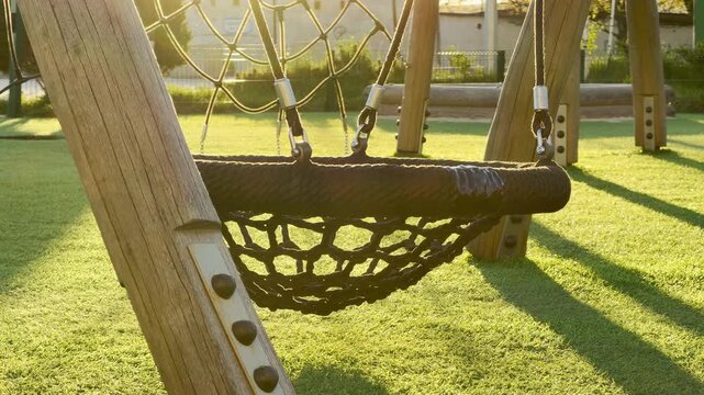 A black rope nest swing rests peacefully under the golden glow of the afternoon sun. This serene scene captures a feeling of quiet rest and nostalgia in an empty neighborhood playground.
