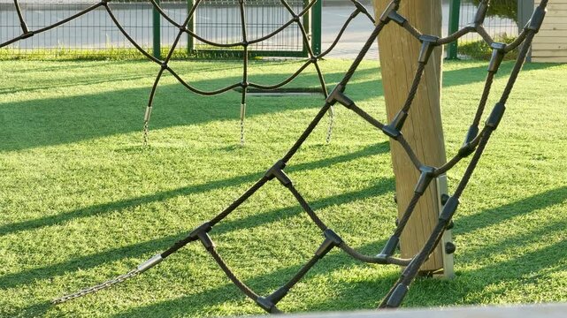 A black rope climbing structure hangs low over a vibrant green lawn in a quiet playground. This peaceful scene captures the simple joy and adventurous spirit of a sunny afternoon outdoors.