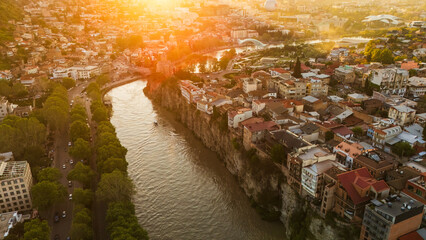 Aerial sunset view of Metekhi district in Tbilisi, Georgia, featuring historic houses on the Kura River cliffs with warm golden hour light over the city © Michele