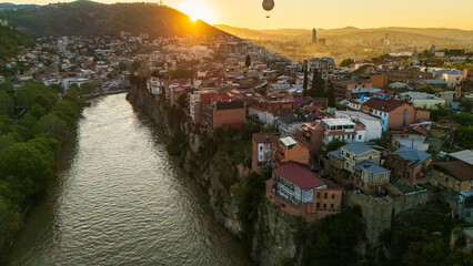 Aerial sunset view of Metekhi district in Tbilisi, Georgia, featuring historic houses on the Kura River cliffs with warm golden hour light over the city © Michele
