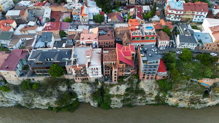 Top-down aerial view of colorful traditional houses perched on the steep Metekhi cliffs above the Kura River in the historic Old Town of Tbilisi, Georgia © Michele