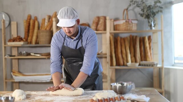 Guy works in bakery as baker, kneads dough, works with flour. Working moment, process of creating croissants in bakery
