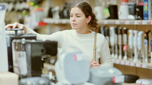 Girl buyer examines coffee machine and decides on purchase. Client in hardware store picks up household appliances. Store of household appliances and household goods, showroom